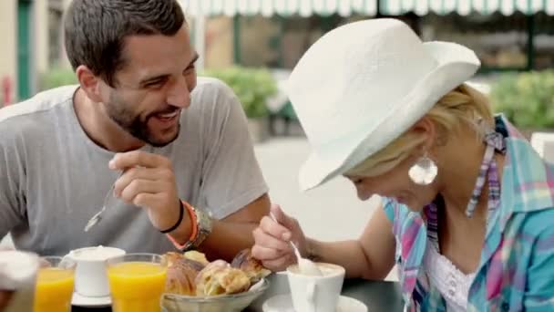 Um jovem e uma jovem mulher tomam café da manhã comendo brioches recheados — Vídeo de Stock