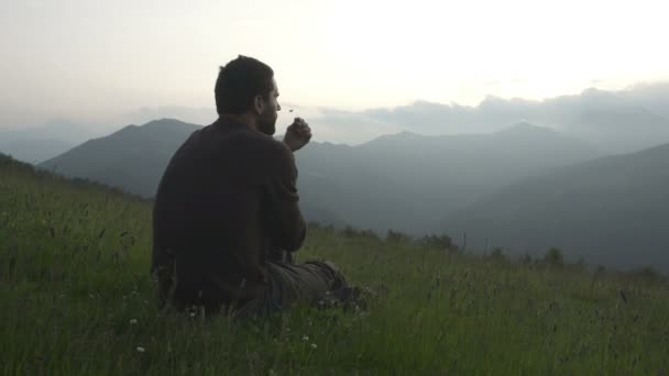 Mladý muž, sedící v trávě se dívá na panorama při západu slunce — Stock video