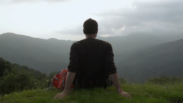 Joven en la montaña con una mochila vintage roja sentada en la hierba — Vídeo de stock