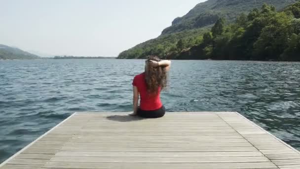 Young woman is seated on a jetty at mergozzo lake in italy — Stock Video