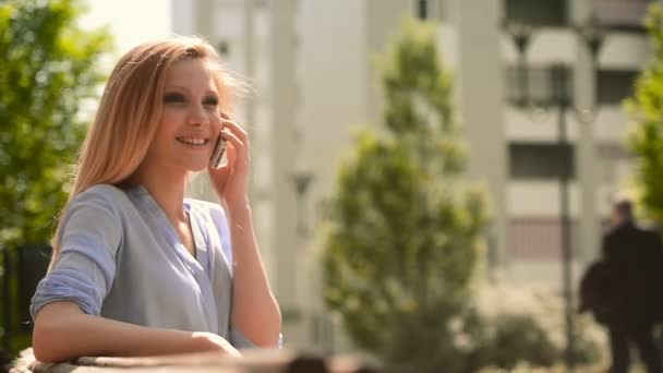Молодая красивая блондинка на смартфоне сидит на скамейке — стоковое видео