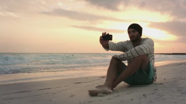 Young beautiful man shoot a selfie on ocean beach seaside at sunrise — Stock Video