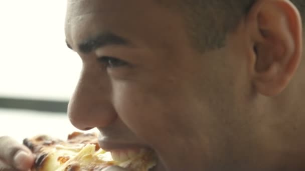 Mooie zwarte jongeman is het eten van een plat brood bij Italiaans restaurant — Stockvideo