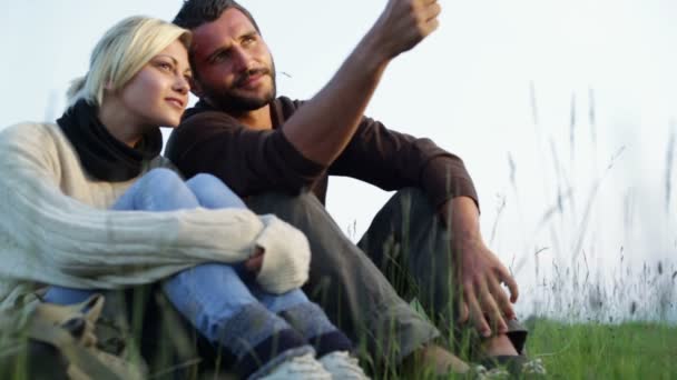 Молодая красивая пара, сидящая на траве, смотрит на панораму — стоковое видео