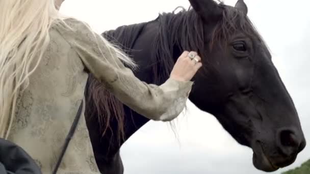 Blonde young woman smiles strokes and hugs black horse — Stock Video