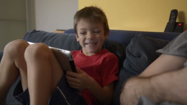 Niño jugar con la tableta en el sofá en casa — Vídeo de stock