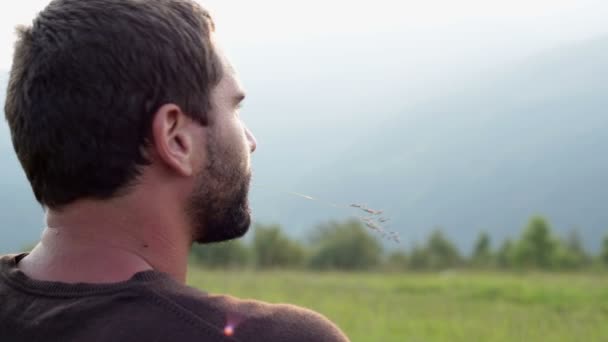Çimenlerin üzerinde oturan genç güzel adam panorama adlı günbatımında izliyor — Stok video