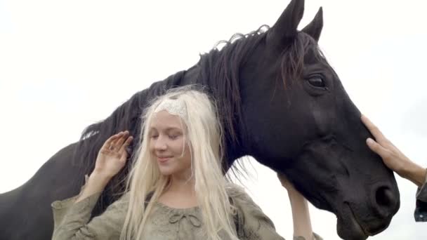 Блондинка улыбается, обнимает черную лошадь. — стоковое видео