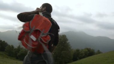 Genç adam bir kırmızı vintage sırt çantası ile açık dağ yolu üzerinde yürüyor