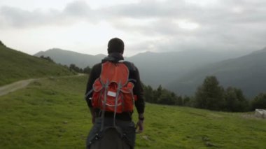 Genç adam bir kırmızı vintage sırt çantası ile açık dağ yolu üzerinde yürüyor