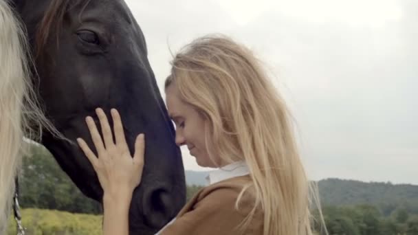 Две молодые женщины улыбаются, обнимают черную лошадь. — стоковое видео
