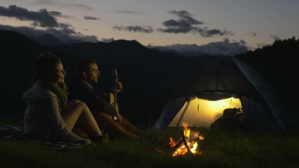 Group of three friends play guitar and sing at camp fire in nature mountain — Stock Video