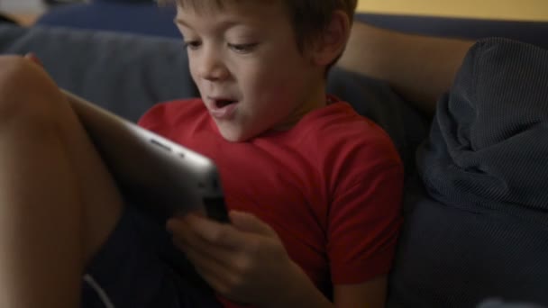 Child play with tablet on sofa at home — Stock Video