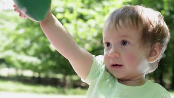 Маленька усміхнена блондинка грає з м'ячем у сонячний літній день у парку — стокове відео