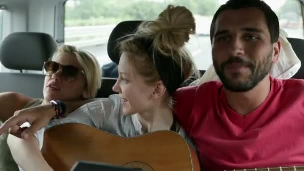 Троє молодих друзів весело співають з гітарою під час подорожі — стокове відео