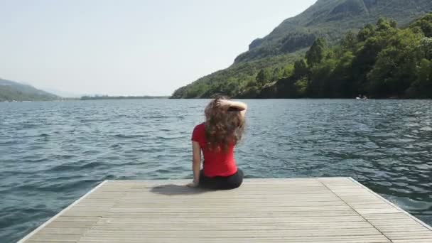 Young woman is seated on a jetty at mergozzo lake in italy in summer day — Stock Video