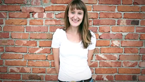 Young smiling woman in front of brick wall — Stock Video