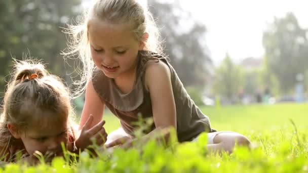 Heureuses soeurs blondes allongées sur l'herbe lisent des contes de fées sur tablette — Video