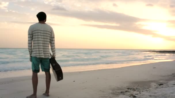 Joven hombre hermoso se levanta mirando al océano en la playa junto al mar — Vídeos de Stock