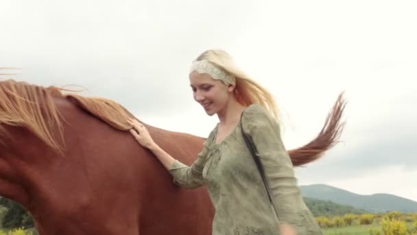 Mujer joven rubia sonríe golpes y abraza caballo marrón — Vídeo de stock