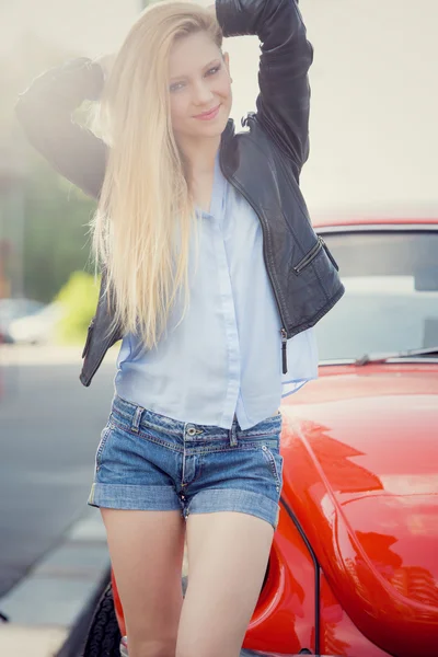 Blonde jonge vrouw met rode oude auto in een stadsgezicht glimlachen — Stockfoto