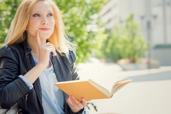 Lächelnde blonde junge Frau liest und studiert in einem Garten — Stockfoto