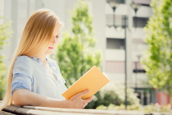 Blonde jonge vrouw lachend lezen en bestuderen in een tuin — Stockfoto