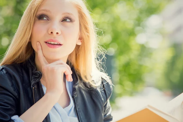 Lächelnde blonde junge Frau liest und studiert in einem Garten — Stockfoto