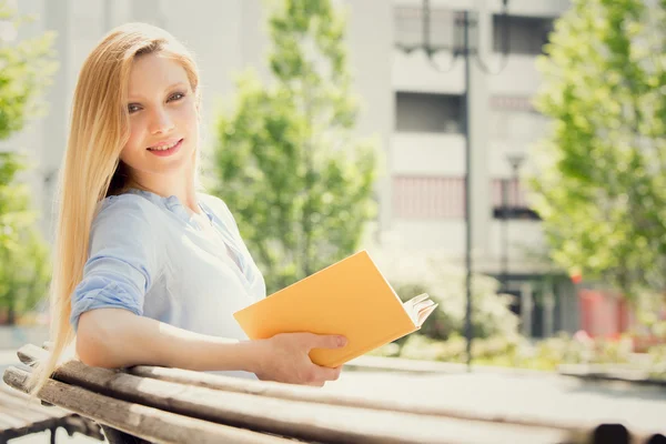 Lächelnde blonde junge Frau liest und studiert in einem Garten — Stockfoto