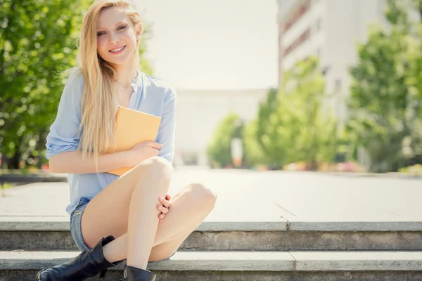 Lächelnde blonde junge Frau mit Buch entspannen in einem Garten — Stockfoto