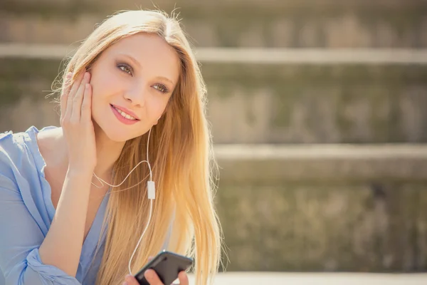 Sonriente rubia joven texto con teléfono relajarse en un paisaje urbano — Foto de Stock