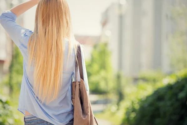 Pelo largo rubia espalda con bolsa en un paisaje urbano verde — Foto de Stock