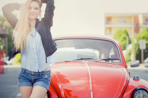 Улыбающаяся блондинка с красной старой машиной в городском пейзаже — стоковое фото