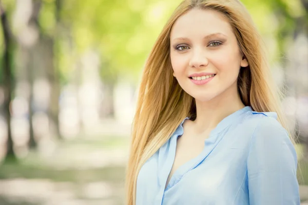 Lachend portret van de blonde jonge vrouw in een groen stadsgezicht — Stockfoto