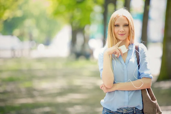 Blonde jonge vrouw met telefoon portret in een groene stadsgezicht glimlachen — Stockfoto