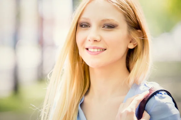 Lachend portret van de blonde jonge vrouw in een groen stadsgezicht — Stockfoto