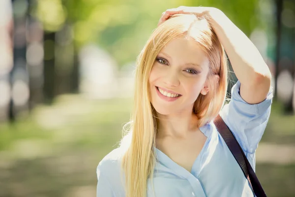 Lächelnde blonde junge Frau im grünen Stadtbild — Stockfoto