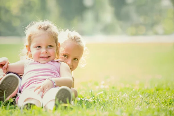 Loira sorrindo irmã jogar em um jardim — Fotografia de Stock