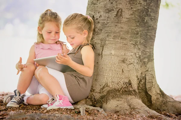 Bionda sorridente sorella giocare con tablet in un giardino — Foto Stock