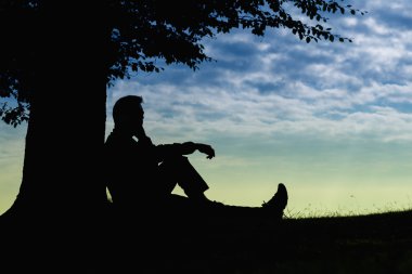 Ağacın altında telefon ile bulutlu gün açık oturan adam siluet
