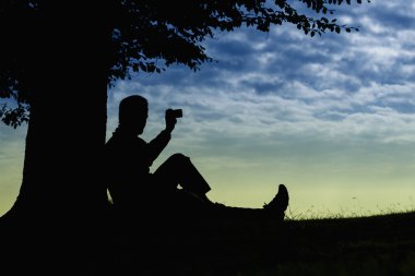 Ağacın altında telefon ile bulutlu gün açık oturan adam siluet