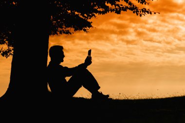 Ağacın altında tablet ile bulutlu gün açık oturan adam siluet