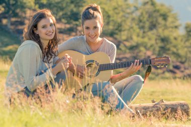 Genç kadın şarkı gitar çalmak arkadaşıyla günbatımı açık