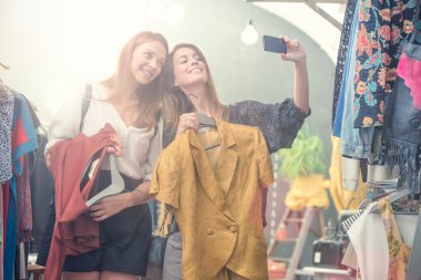 İki gülen arkadaş giyim mağazasında eğleniyor.