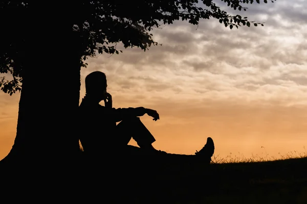 Silhouette homme assis sous l'arbre avec téléphone par jour nuageux en plein air — Photo