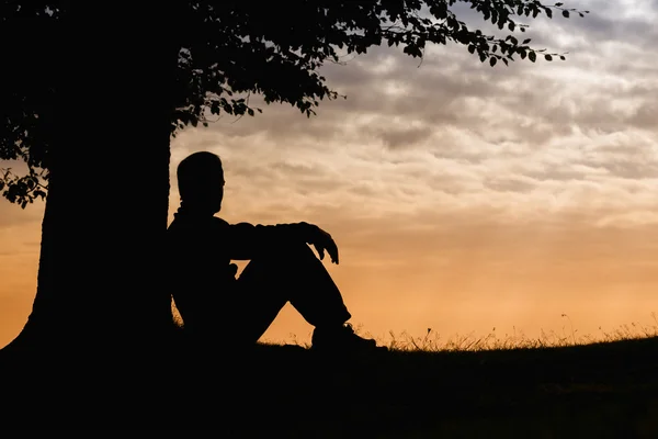 Silueta muž sedí pod stromem na zamračený den venkovní — Stock fotografie