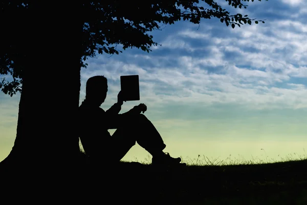 Ember sziluettje tabletta felhős napon kültéri fa alatt ül — Stock Fotó