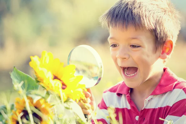 Улыбающийся ребенок играет с лупой в саду — стоковое фото