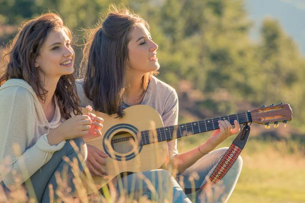 Jovem mulher cantar tocando guitarra com amigo no pôr do sol ao ar livre — Fotografia de Stock