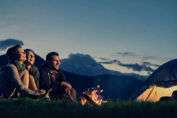 Tre amici in campeggio con fuoco sulla montagna al tramonto — Foto Stock